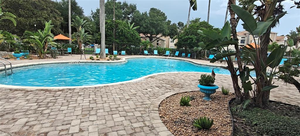 A swimming pool with a brick paver deck is surrounded by lush tropical landscaping — 7220 WESTPOINTE BLVD UNIT 1429, ORLANDO, FL