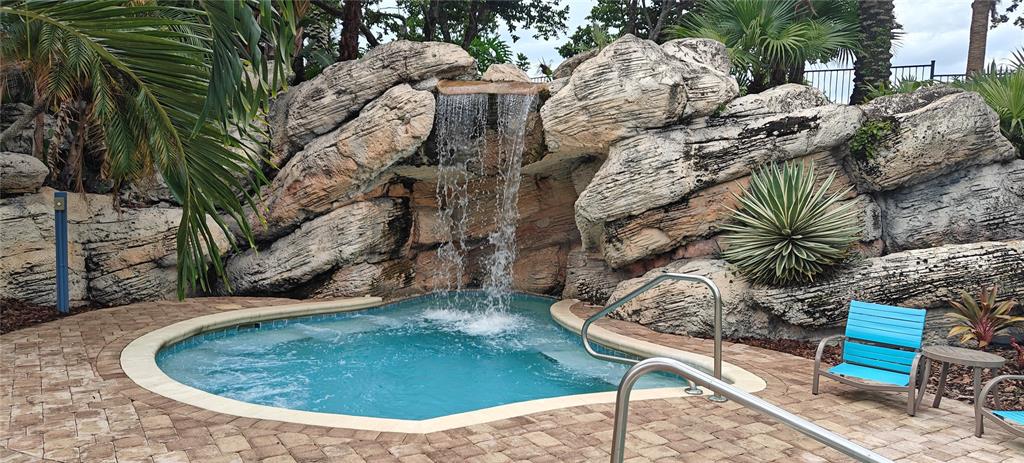 A small swimming pool features a stone waterfall and a surrounding paver patio — 7220 WESTPOINTE BLVD UNIT 1429, ORLANDO, FL
