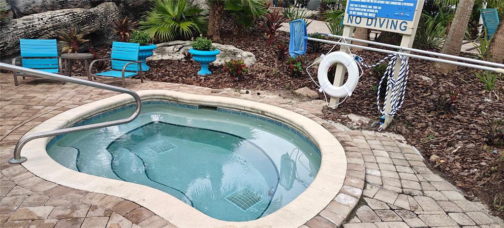 A small outdoor hot tub sits on a paved patio near blue chairs and landscaping — 7220 WESTPOINTE BLVD UNIT 1429, ORLANDO, FL