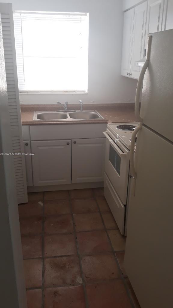 A small kitchen features white cabinets, a double sink, and a white stove — 6520 Winfield Blvd # 103, Margate FL 33063, MARGATE, FL