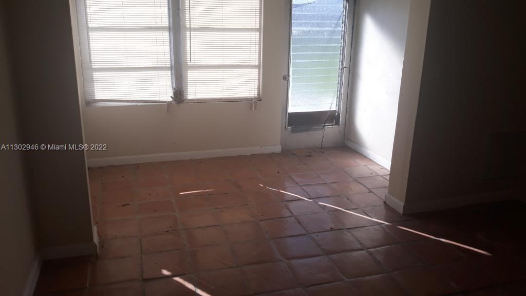 An empty room features terracotta tile flooring, white walls, and a glass-paned exterior door — 6520 Winfield Blvd # 103, Margate FL 33063, MARGATE, FL