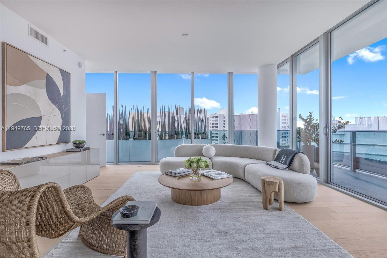 A modern living room features a curved sofa, wooden coffee table, and floor-to-ceiling windows — 9201 E Bay Harbor Dr, Bay Harbor Islands FL 33154, BAY HARBOR ISLANDS, FL