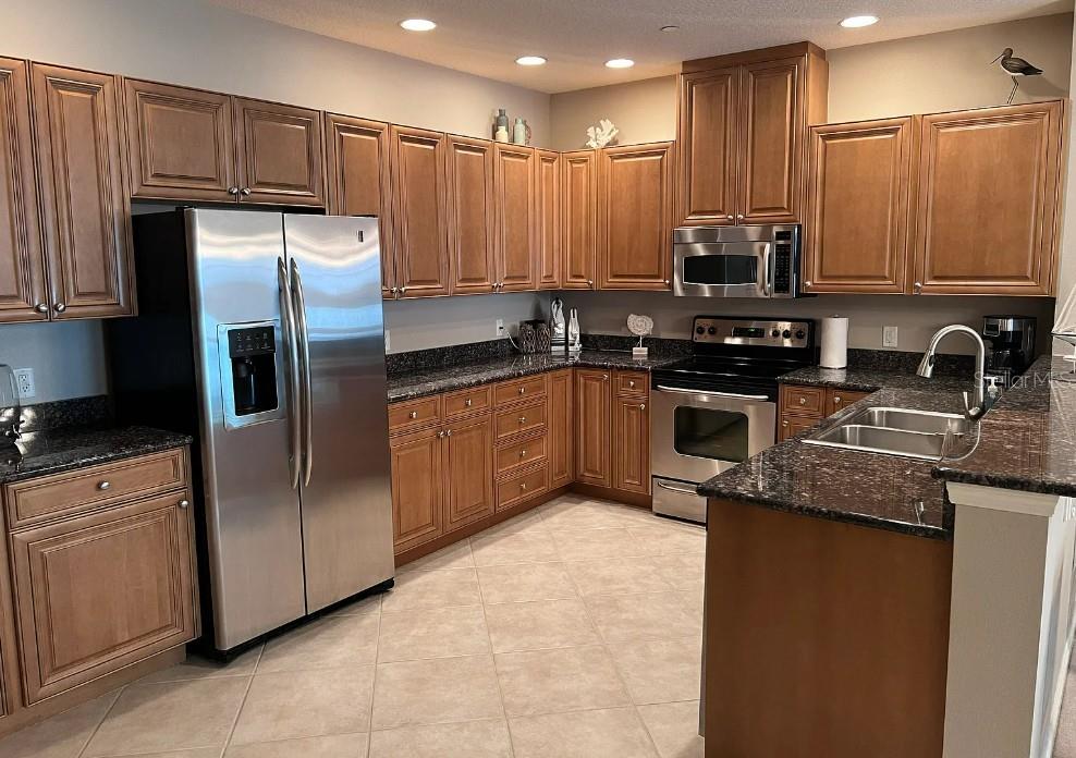 A kitchen features wood cabinets, dark granite countertops, stainless steel appliances, and tile flooring — 505 MANDALAY AVENUE UNIT 72, CLEARWATER BEACH, FL