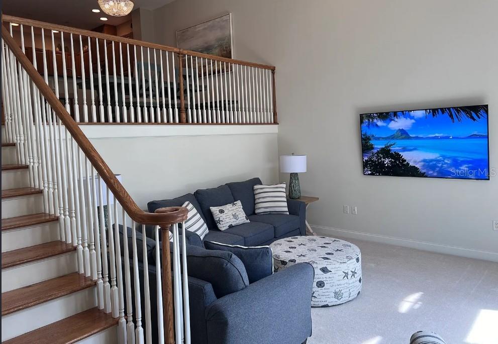 A living room with a blue sofa, a round ottoman, and a staircase with railings — 505 MANDALAY AVENUE UNIT 72, CLEARWATER BEACH, FL