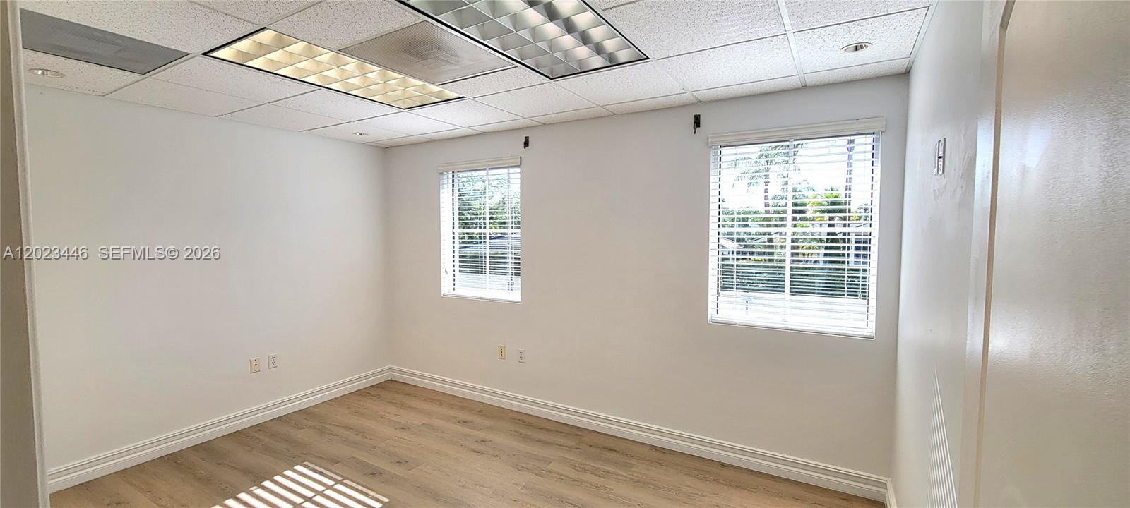 An empty office room features white walls, wood-look flooring, and a drop ceiling with lights — 7765 SW 87th Ave # 207A, Miami FL 33173, MIAMI, FL