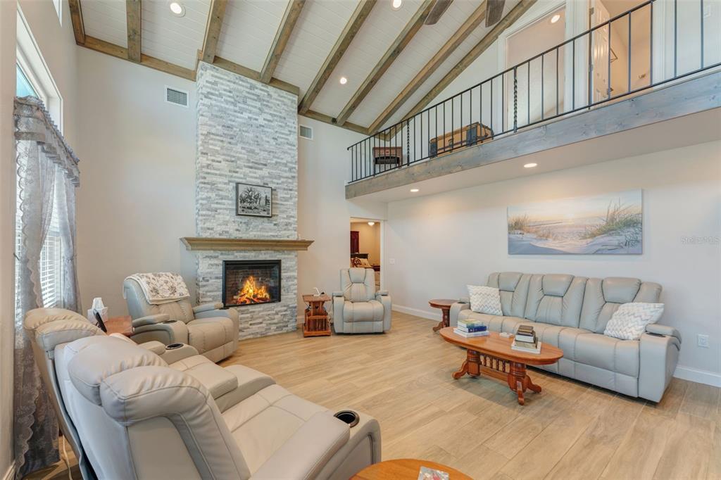 A spacious living room with a stone fireplace, vaulted wood-beam ceiling, and a loft balcony — 3502 BAHIA VISTA STREET, SARASOTA, FL