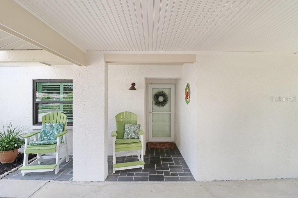 A covered porch features a white door, two green chairs, and dark tiled flooring — 9247 GOLF VIEW DRIVE UNIT 9247, NEW PORT RICHEY, FL