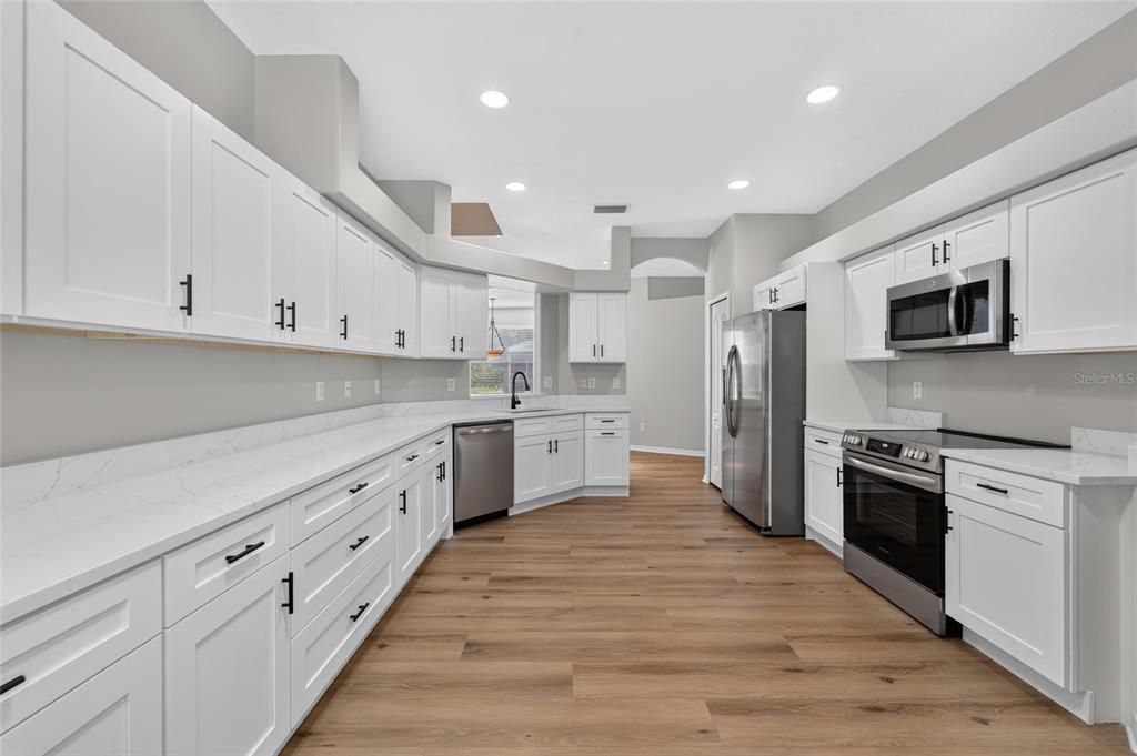 A kitchen features white cabinets, quartz countertops, stainless steel appliances, and wood-look flooring — 21744 WAVERLY SHORES LANE, LAND O LAKES, FL