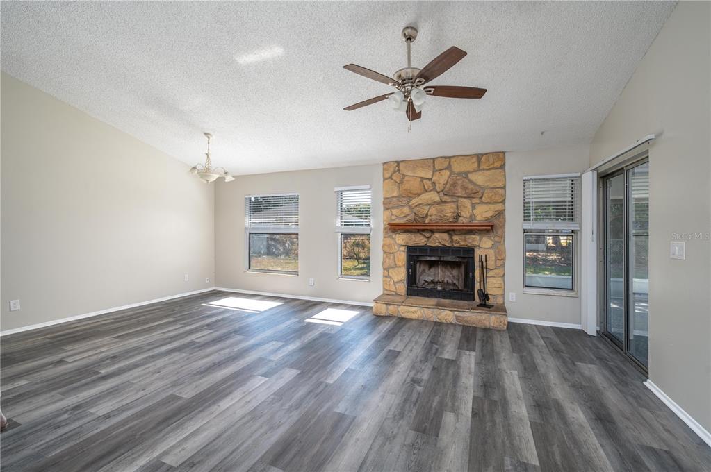 A living room features gray wood-look flooring, a stone fireplace, and a ceiling fan — 3406 FOX RIDGE STREET, WINTER HAVEN, FL