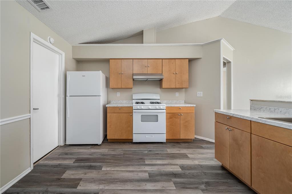 A kitchen features light wood cabinets, white appliances, and gray wood-look flooring — 3406 FOX RIDGE STREET, WINTER HAVEN, FL
