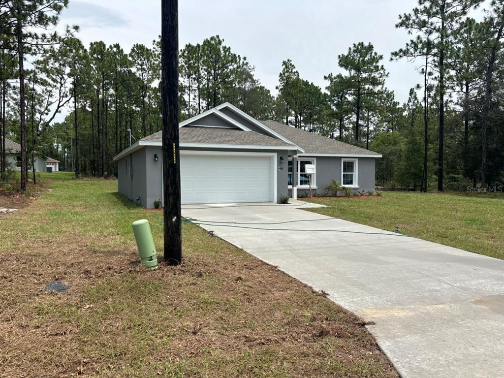 A gray, single-story house with a two-car garage sits on a wooded lot — 9345 N CORTLANDT DRIVE, DUNNELLON, FL
