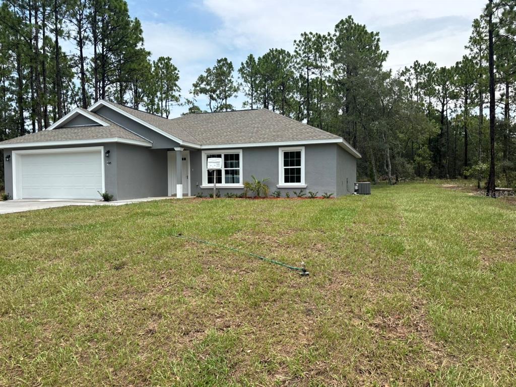 A single-story gray house with a two-car garage sits on a grassy lot — 9345 N CORTLANDT DRIVE, DUNNELLON, FL