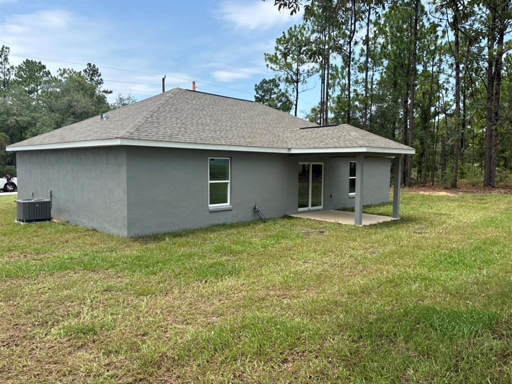 The rear exterior of a gray stucco house features a covered patio and a yard — 9345 N CORTLANDT DRIVE, DUNNELLON, FL