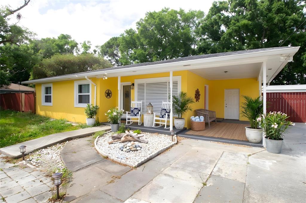 A bright yellow single-story house features a covered porch, white rocking chairs, and landscaping — 7716 E COMANCHE AVENUE, TAMPA, FL