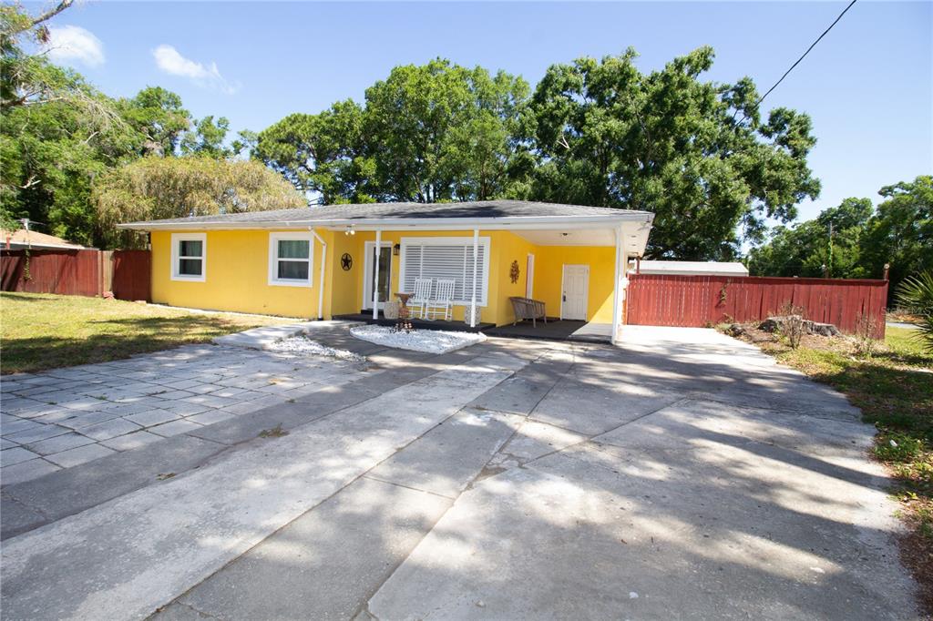 A yellow single-story house with a concrete driveway and a covered front porch — 7716 E COMANCHE AVENUE, TAMPA, FL