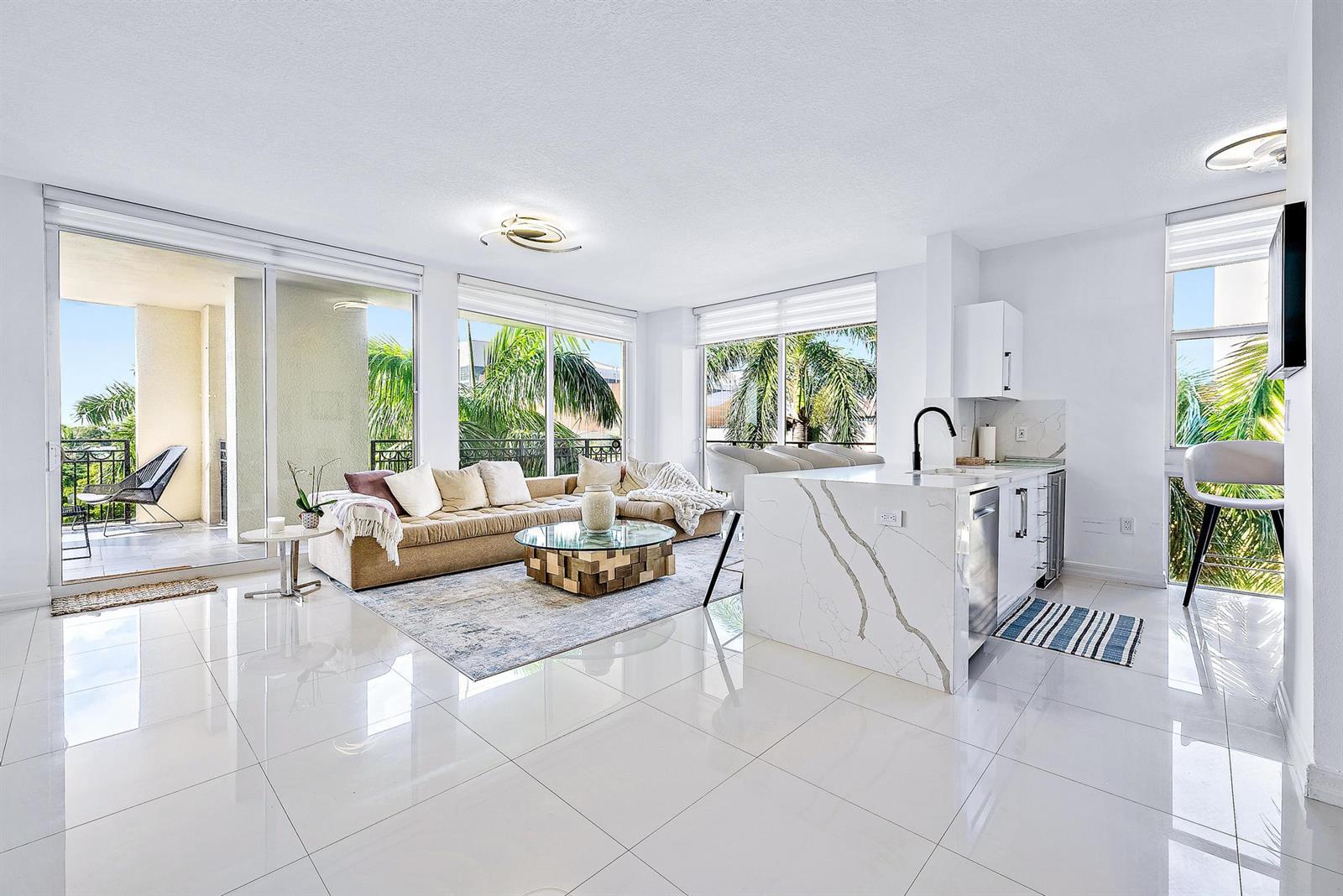 A bright, open-concept living room and kitchen featuring white tile floors and a balcony — 550 Okeechobee Boulevard # 422, West Palm Beach FL 33401, WEST PALM BEACH, FL