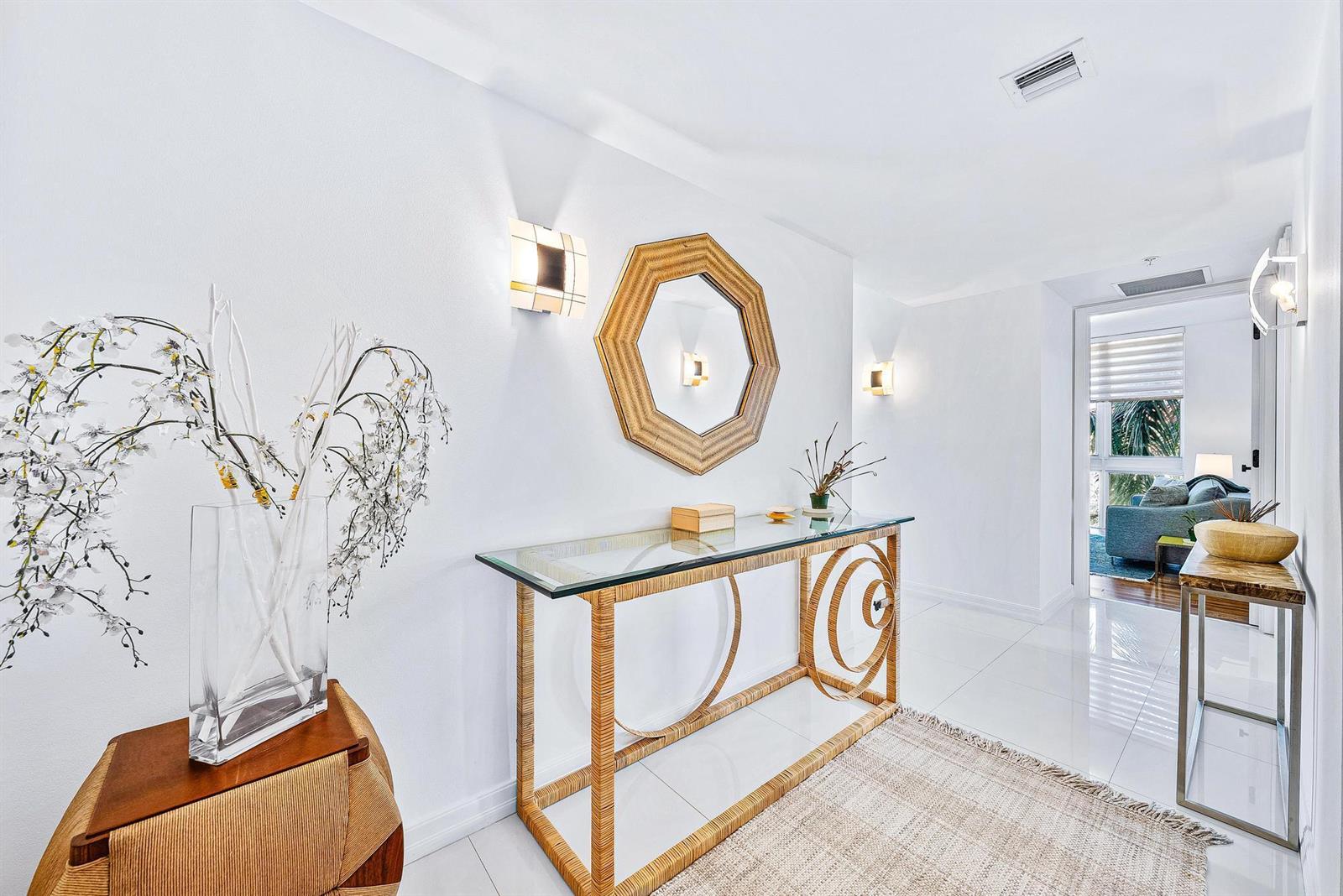 A bright entryway features white walls, tile flooring, a glass console table, and a mirror — 550 Okeechobee Boulevard # 422, West Palm Beach FL 33401, WEST PALM BEACH, FL