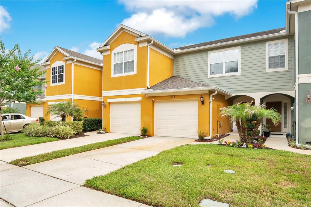 A two-story townhouse with yellow and green siding, two garage doors, and a front lawn — 1122 BERKMAN CIRCLE, SANFORD, FL