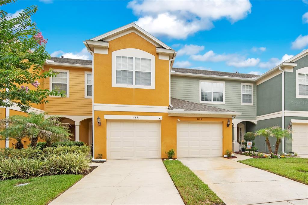 A two-story townhouse with yellow and green siding, two garage doors, and concrete driveways — 1122 BERKMAN CIRCLE, SANFORD, FL