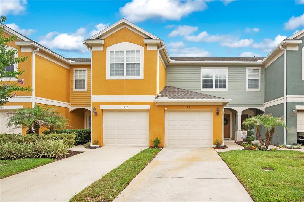 A two-story townhouse exterior with two garage doors, yellow and green siding, and a driveway — 1122 BERKMAN CIRCLE, SANFORD, FL