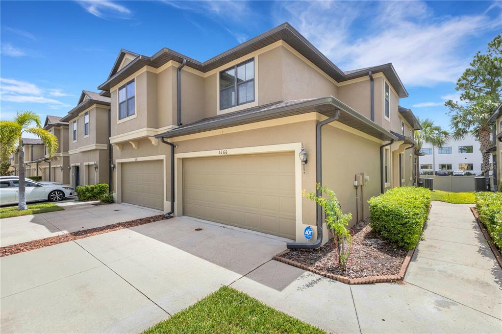 A two-story townhouse exterior features a beige stucco facade, a two-car garage, and a sidewalk — 5166 BAY ISLE CIRCLE, CLEARWATER, FL