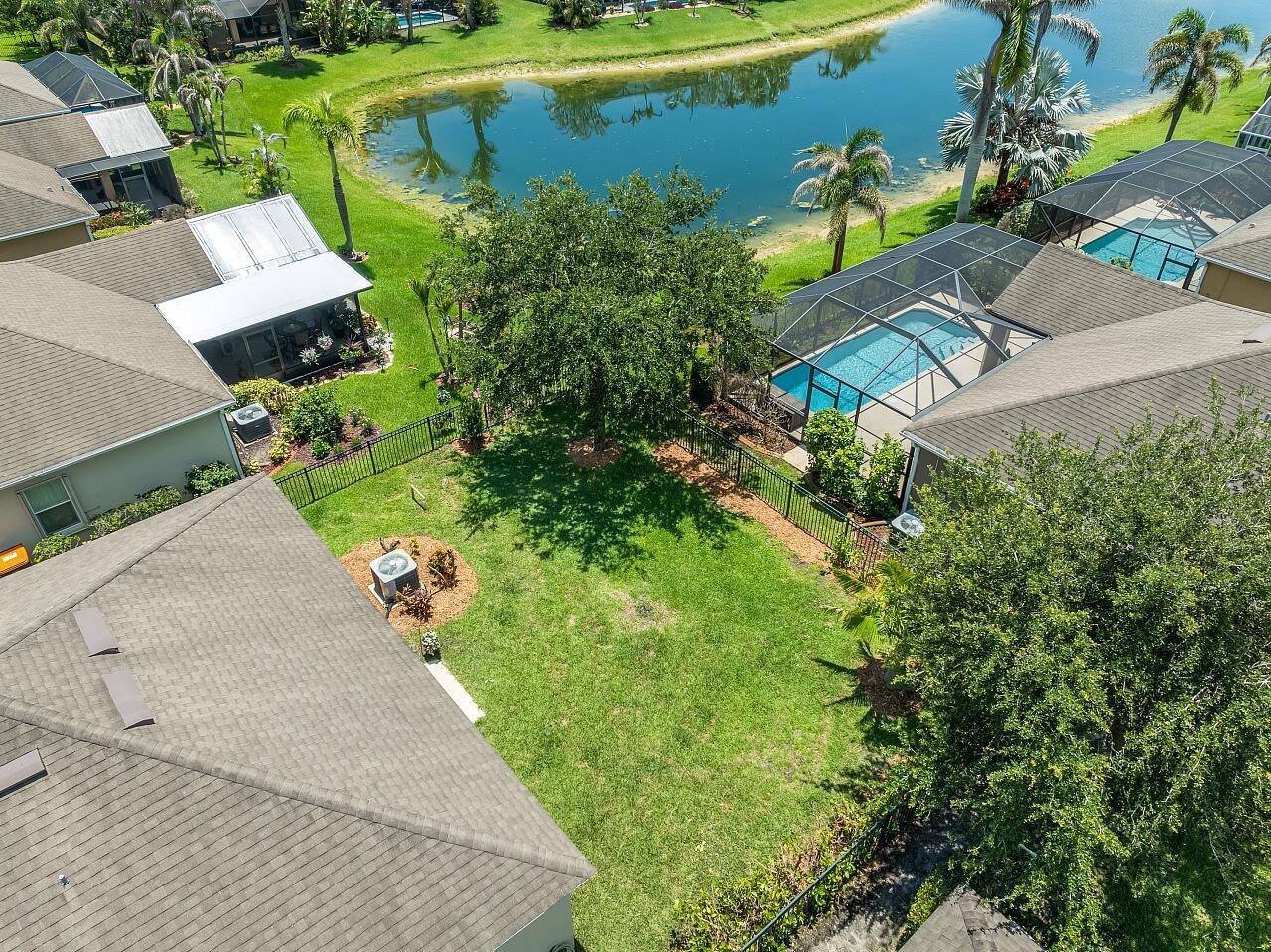 An aerial view shows a backyard with a pool, lawn, and lake in a neighborhood — 8110 Westfield Circle, Vero Beach FL 32966, VERO BEACH, FL