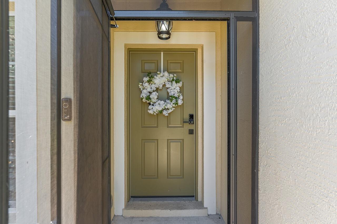 A green front door with a white floral wreath sits inside a screened entryway — 8110 Westfield Circle, Vero Beach FL 32966, VERO BEACH, FL