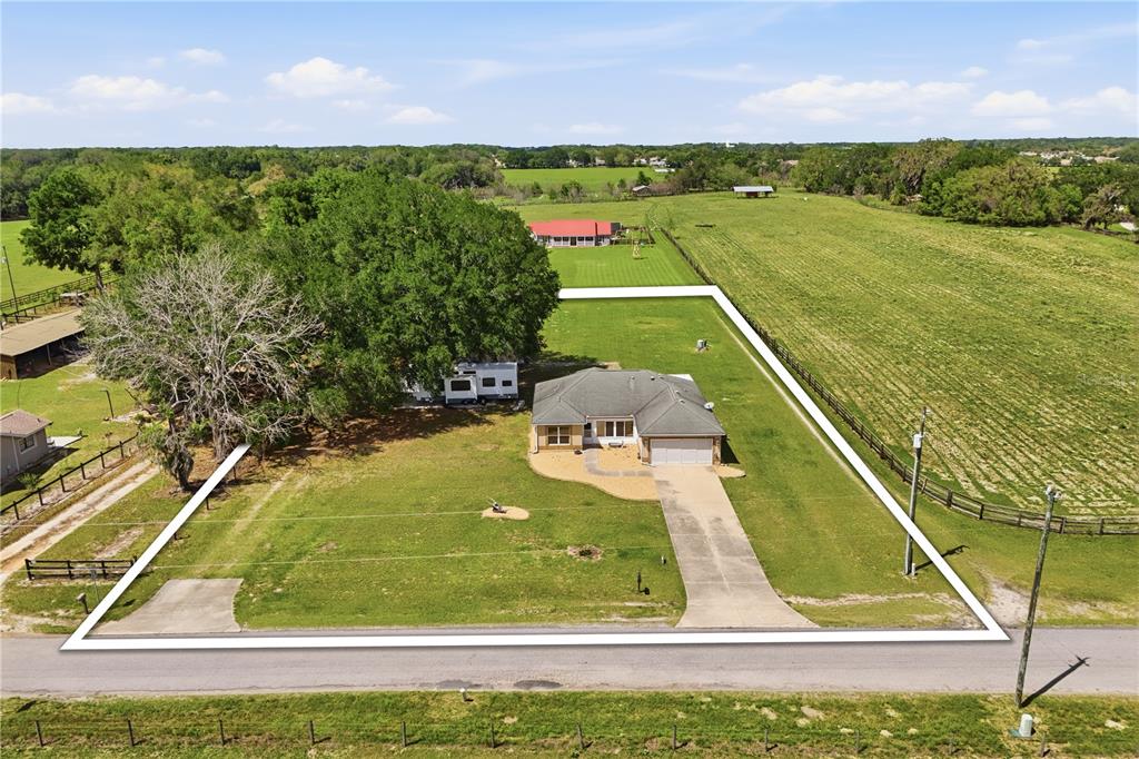 An aerial view shows a single-story house with a driveway on a grassy lot — 7411 SE 180TH STREET, OXFORD, FL