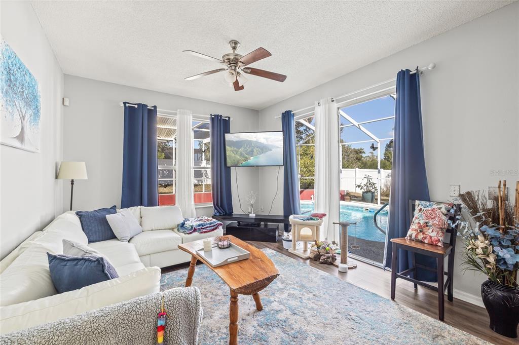 A living room features a white sectional sofa, a wooden coffee table, and a pool view — 6401 GRAPEWOOD ROAD, SPRING HILL, FL