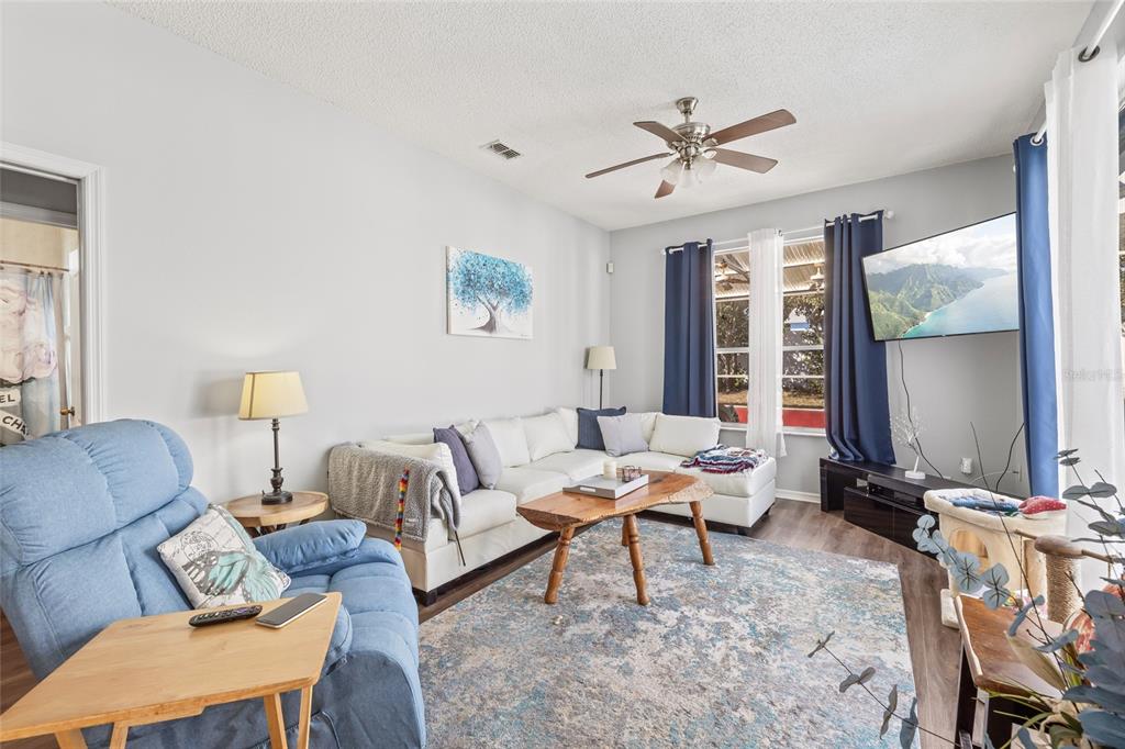 A living room features a blue recliner, a white sectional sofa, and a wall-mounted television — 6401 GRAPEWOOD ROAD, SPRING HILL, FL