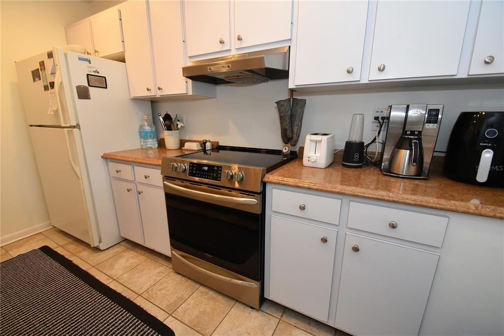A kitchen features white cabinets, stainless steel appliances, and tan countertops over tiled flooring — 1712 GLENHOUSE DRIVE UNIT GL417, SARASOTA, FL