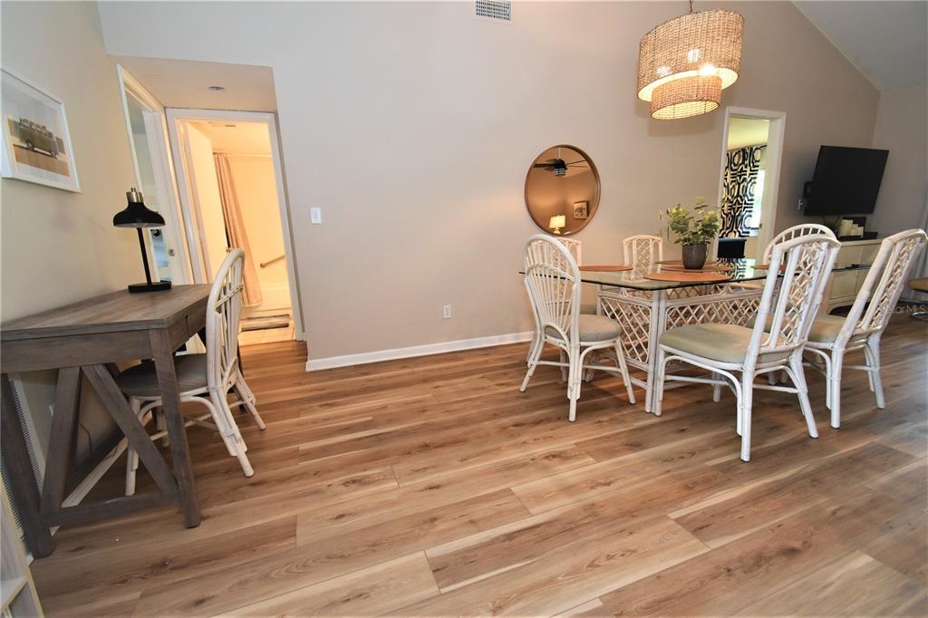 A dining area and workspace feature wood-look flooring, white wicker chairs, and a glass table — 1712 GLENHOUSE DRIVE UNIT GL417, SARASOTA, FL
