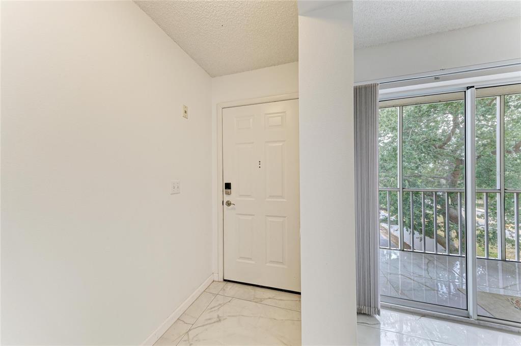An entryway features white walls, marble-look tile flooring, a white door, and a sliding glass door — 3980 IRONWOOD CIRCLE UNIT 301, BRADENTON, FL