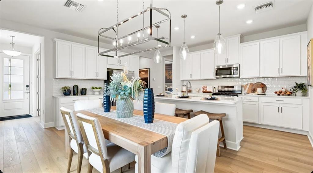 A bright kitchen and dining area features white cabinetry, a wooden table, and pendant lighting — 26141 CAMOGLI COURT, ENGLEWOOD, FL