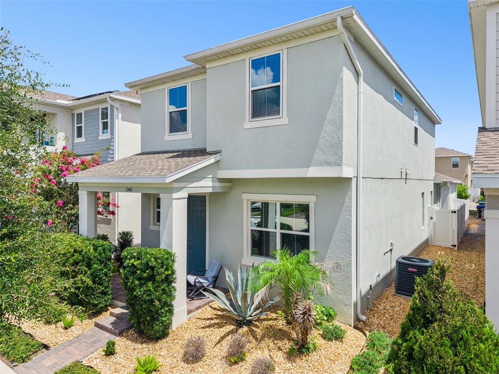 A two-story light-colored house with a front porch, landscaping, and a side air conditioning unit — 15411 GILLIGAN COURT, WINTER GARDEN, FL