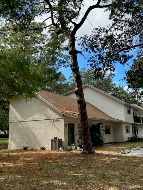 A two-story stucco building with a brown shingled roof stands behind a tall pine tree — 2122 BRADFORD STREET UNIT 521, CLEARWATER, FL