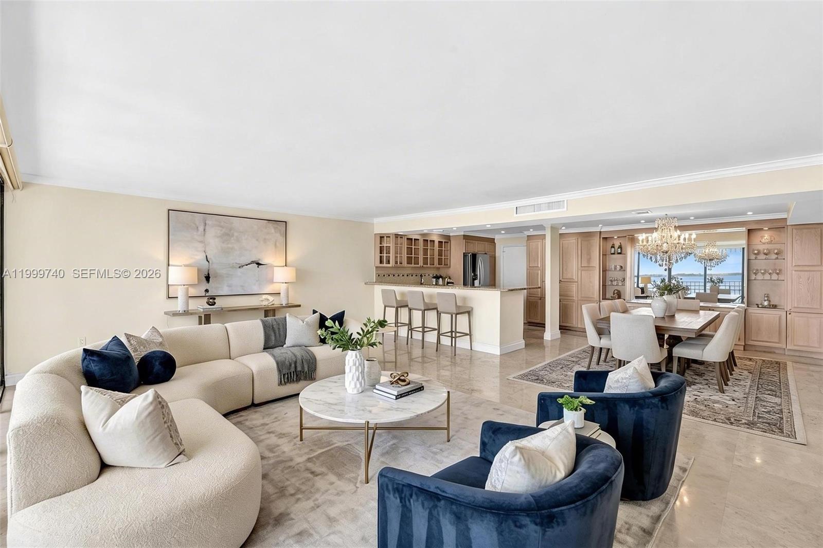 A spacious open-concept living and dining area features light-colored furniture, marble floors, and water views — 2 Grove Isle Dr # B805, Miami FL 33133, MIAMI, FL