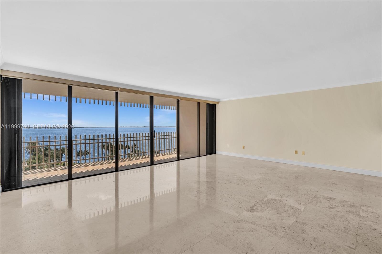 An empty room with polished stone floors and a large sliding glass door overlooking water — 2 Grove Isle Dr # B805, Miami FL 33133, MIAMI, FL