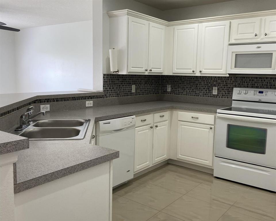A kitchen features white cabinets, gray countertops, a tiled backsplash, and white appliances — 2444 HASSONITE STREET, KISSIMMEE, FL