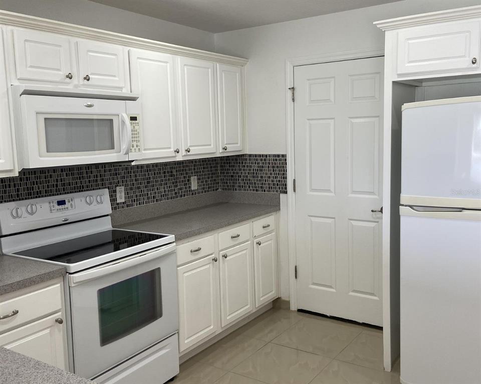 A kitchen features white cabinets, a microwave, a stove, a refrigerator, and a tiled backsplash — 2444 HASSONITE STREET, KISSIMMEE, FL