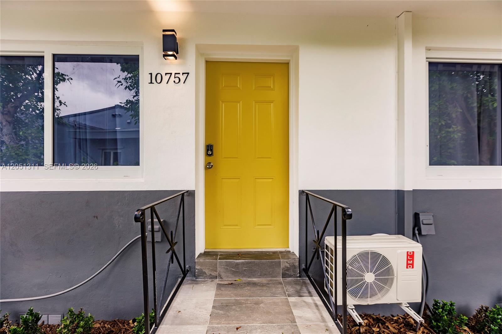 A bright yellow front door is centered between two windows on a two-tone exterior wall — 10757 NE 2 Ct # 0, Miami FL 33161, MIAMI, FL
