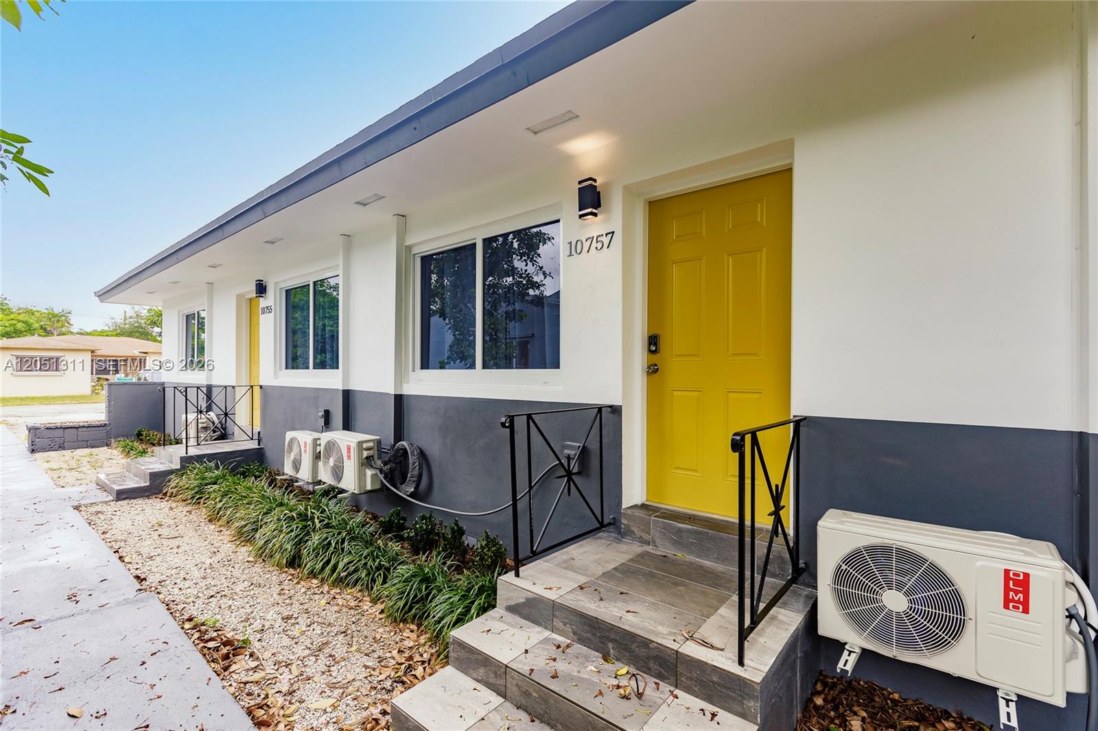The exterior of a duplex features white and gray walls, yellow doors, and outdoor AC units — 10757 NE 2 Ct # 0, Miami FL 33161, MIAMI, FL