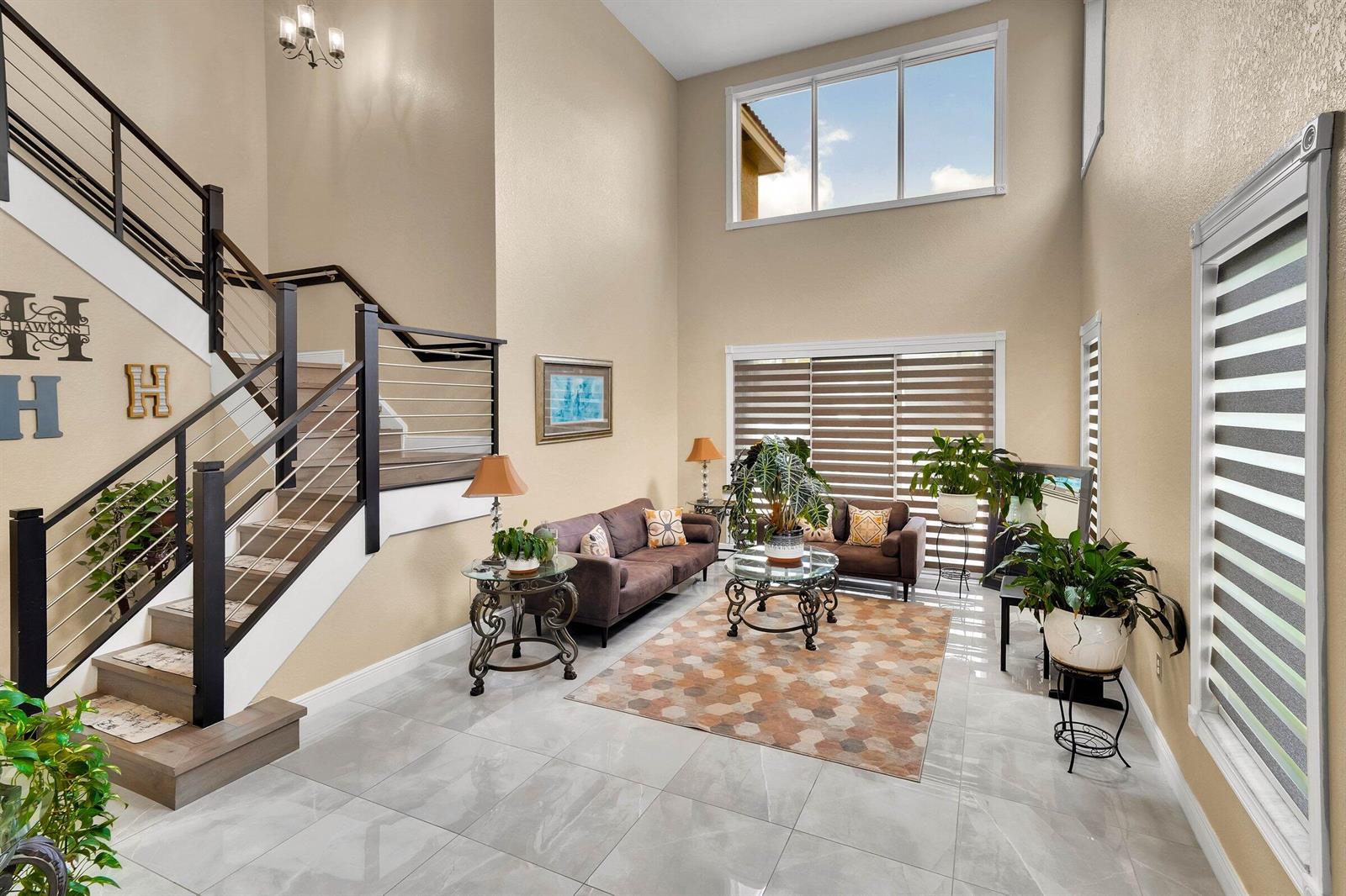 A high-ceilinged living room features a staircase, tile flooring, and large windows with blinds — 16254 SW 18th Place, Miramar FL 33027, MIRAMAR, FL