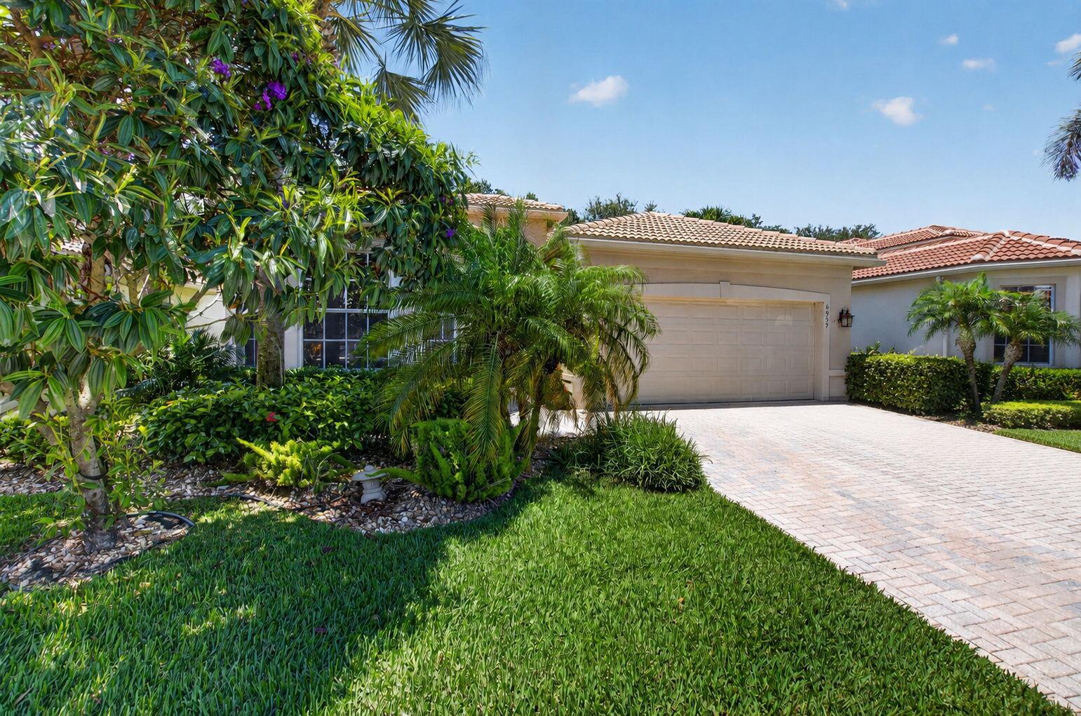 A beige house with a tiled roof, a paved driveway, and lush landscaping in front — 6959 Imperial Beach Circle, Delray Beach FL 33446, DELRAY BEACH, FL