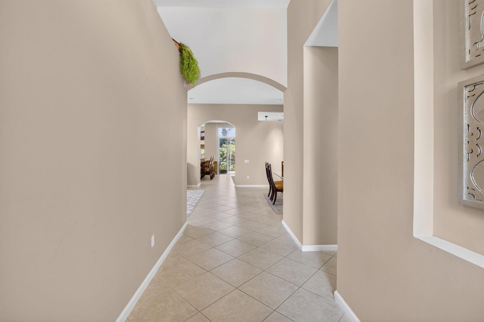 A beige hallway with tiled floors leads through arched doorways toward a dining area — 6959 Imperial Beach Circle, Delray Beach FL 33446, DELRAY BEACH, FL