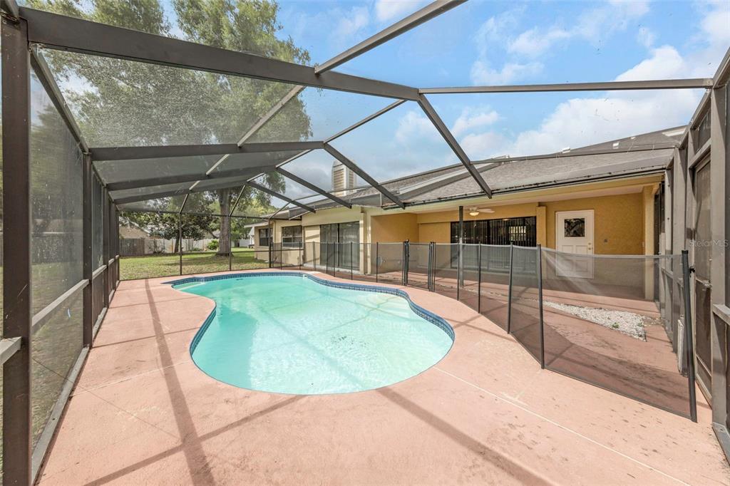 A screened-in patio features a swimming pool and a safety fence on a concrete deck — 3334 BRIAN ROAD N, PALM HARBOR, FL