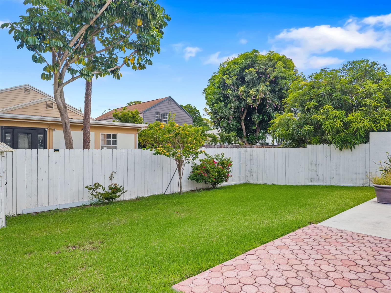 A backyard features a green lawn, a white wooden fence, and a paved patio area — 6196 Azalea Circle, West Palm Beach FL 33415, WEST PALM BEACH, FL