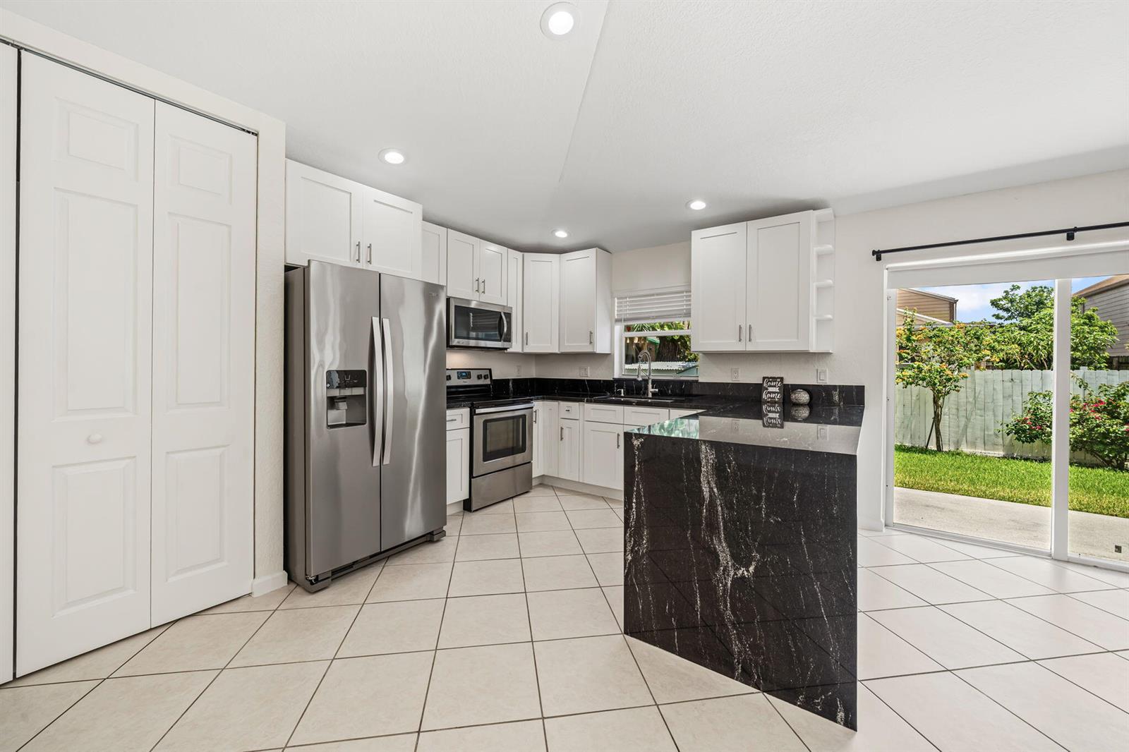 A kitchen with white cabinets, stainless steel appliances, black granite countertops, and tile flooring — 6196 Azalea Circle, West Palm Beach FL 33415, WEST PALM BEACH, FL