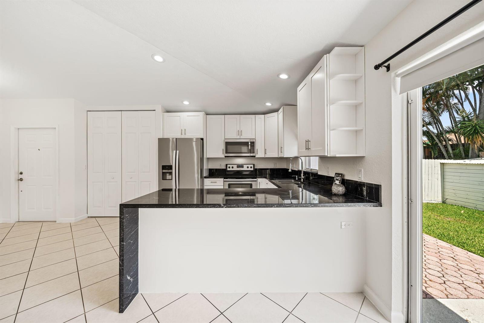 A kitchen features white cabinets, black countertops, stainless steel appliances, and tile flooring — 6196 Azalea Circle, West Palm Beach FL 33415, WEST PALM BEACH, FL