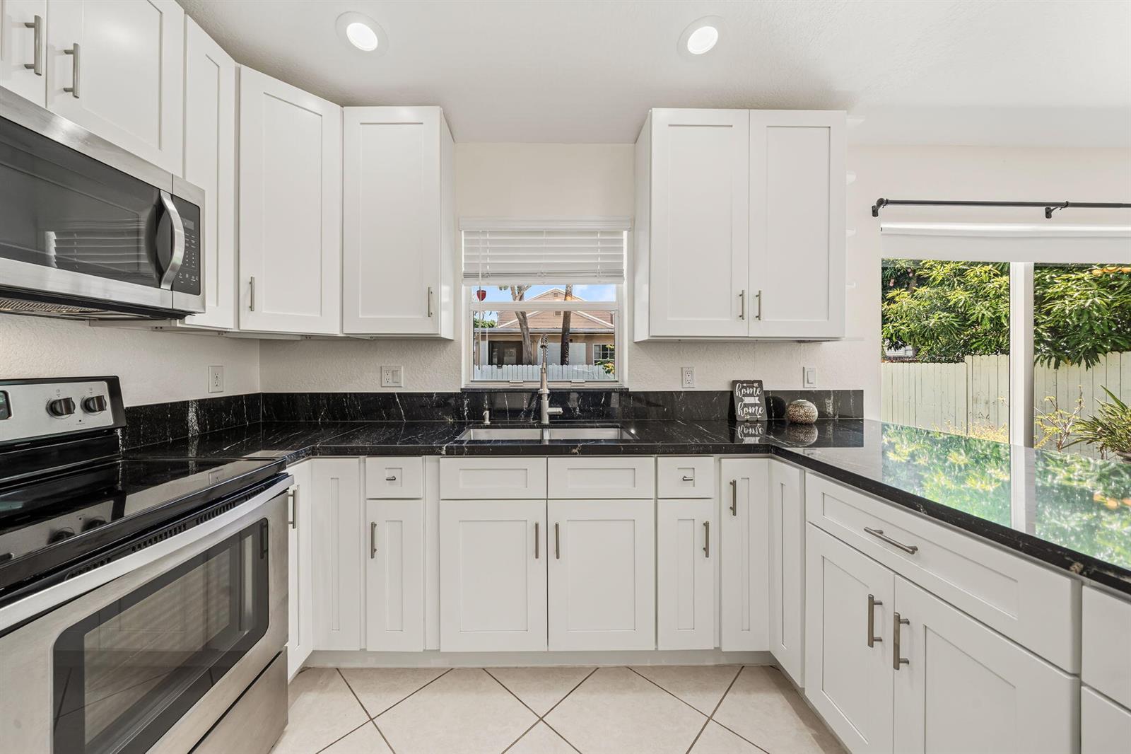 A kitchen features white cabinets, black countertops, stainless steel appliances, and a window above the sink — 6196 Azalea Circle, West Palm Beach FL 33415, WEST PALM BEACH, FL